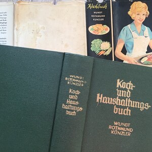 K&ouml;nnte beinhalten: Eine Sammlung alter Kochb&uuml;cher. Das Hauptbuch ist dunkelgr&uuml;n mit goldener Schrift, die "Koch und Haushaltungsbuch" und "WUNDT ROTHMUND K&Uuml;NZLER" lautet. Weitere B&uuml;cher sind sichtbar, darunter eines mit einer Frau auf dem Cover.