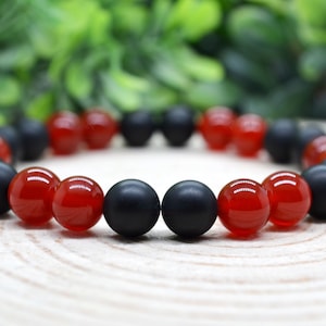 May include: A bracelet made of black and red beads. The bracelet is made of round beads, with the black beads being matte and the red beads being shiny.