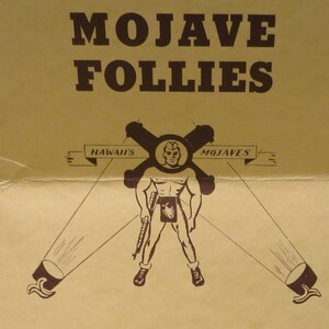 May include: A vintage poster advertising "Mojave Follies" with a cartoon illustration of a man in a military cap holding a rifle. The poster features the text "Hawaii's" and "Mojaves" on either side of the man.