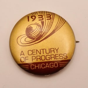 May include: A vintage round button with a gold background and brown text and graphics. The text reads "1933", "A Century of Progress", and "Chicago". The button has a pin on the back.