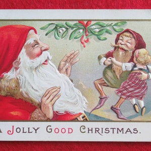May include: A vintage Christmas postcard featuring a jolly Santa Claus with a white beard and red hat, laughing as he watches a couple of elves dance under a sprig of mistletoe. The text on the postcard reads "A Jolly Good Christmas."