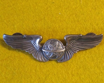 May include: A silver aviator wings badge with a globe and compass design in the center.