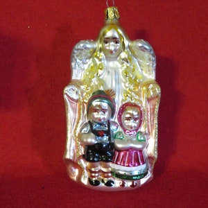 May include: A glass Christmas ornament featuring an angel with wings, holding two children in front of her. The angel is wearing a white gown and has blonde hair. The children are wearing traditional German clothing. The ornament is decorated with gold glitter.