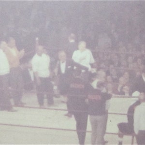 May include: A group of people standing in a room, some wearing white shirts and others wearing dark suits. The room is dimly lit and there are many people in the background.