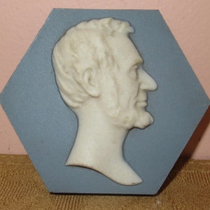 May include: A white ceramic bust of Abraham Lincoln in profile, set against a blue hexagonal background.