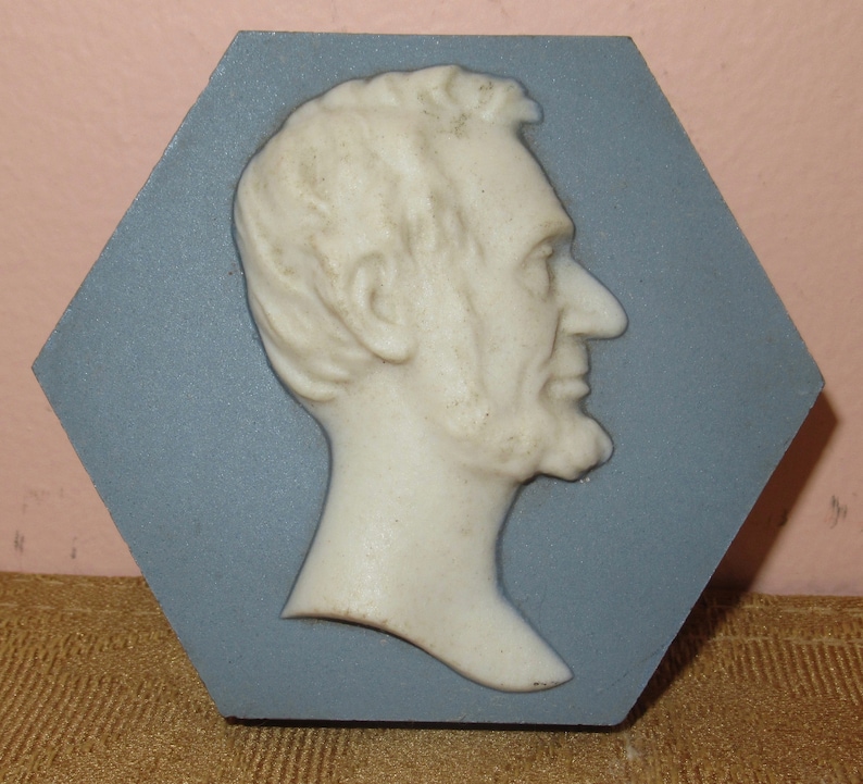 May include: A white ceramic bust of Abraham Lincoln in profile, set against a blue hexagonal background.