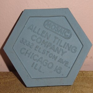 May include: A grey hexagonal tile with the text "Allen Tiling Company 3232 Elston Ave. Chicago Ill." and a smaller circle with the text "Mosaic" in the centre.