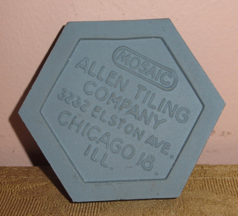 May include: A grey hexagonal tile with the text "Allen Tiling Company 3232 Elston Ave. Chicago Ill." and a smaller circle with the text "Mosaic" in the centre.
