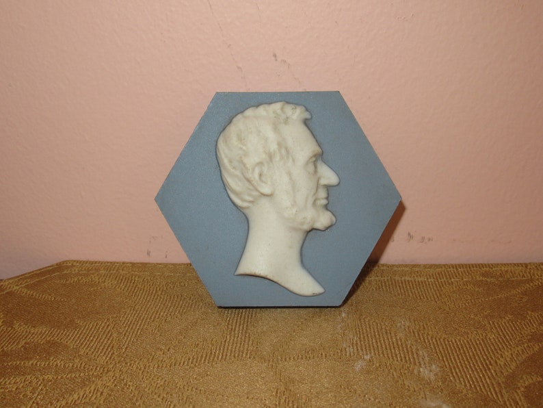 May include: A blue hexagonal ceramic plaque featuring a white bas-relief sculpture of Abraham Lincoln's profile.