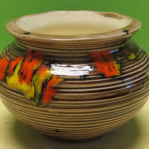 May include: A brown ceramic planter with a striped pattern and orange, yellow, and black painted designs.