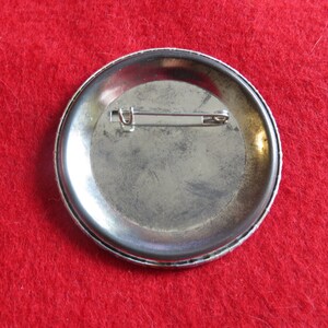May include: The back of a silver button pin with a metal pin back.