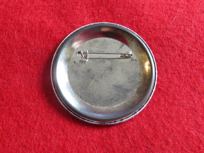May include: The back of a silver button pin with a metal pin back.