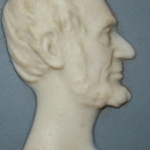 May include: A white porcelain cameo of a man's profile, with a detailed face and hair, set against a blue background.