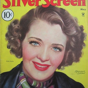 May include: A vintage magazine cover featuring a woman with short, curly hair. The cover is yellow with the title "Silver Screen" in red and white lettering. The woman is wearing a dark jacket with a plaid scarf. The text "The TEN BEST STARS For A Desert Island" is at the top of the cover. The magazine is from May 1948.