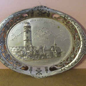May include: A silver-colored metal tray with an embossed image of the Belgian Village from the 1933-1934 World's Fair in Chicago. The tray has a decorative, openwork border.