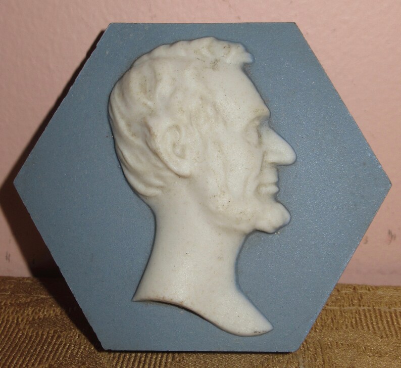May include: A white ceramic bust of Abraham Lincoln in profile, mounted on a blue hexagonal tile.