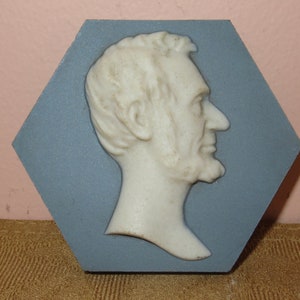 May include: A white ceramic bust of Abraham Lincoln in profile, set against a blue hexagonal tile.