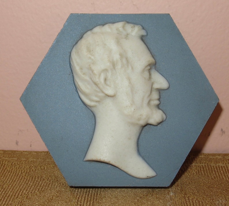 May include: A white ceramic bust of Abraham Lincoln in profile, set against a blue hexagonal tile.