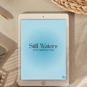 Könnte beinhalten: Ein weißes Tablet mit dem Text "Still Waters" und "An Ever Selah Prayer Guide" auf hellblauem Hintergrund. Das Tablet liegt auf einer neutralfarbenen Oberfläche, im Hintergrund befinden sich ein Stift, eine kleine Holzschale und ein geflochtener Korb.