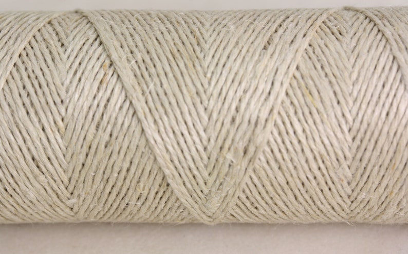 May include: A close-up of a spool of natural-colored twine. The twine is tightly wound and has a slightly rough texture.
