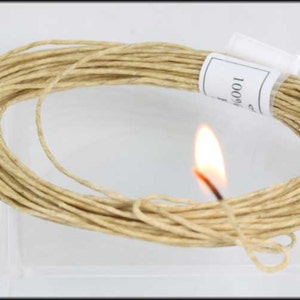 May include: A close-up of a reel of natural beige paper twine with a lit match held next to it. The reel is labelled "100% Cotton".