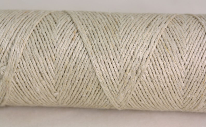 May include: A close-up of a spool of natural-colored twine. The twine is tightly wound and has a smooth, even texture.