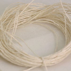 May include: A close-up of a spool of natural white twine. The twine is made of thin, tightly wound strands of natural fiber.
