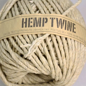 Puede incluir: Una bola de cuerda de cáñamo natural con una etiqueta de papel marrón que dice "HEMP TWINE 200 LB TEST STRENGTH (4mm) 141 FEET (43 M) 100% HEMP"
