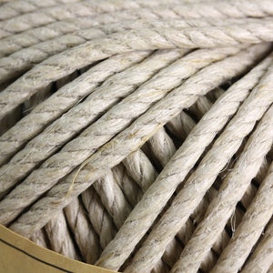 Puede incluir: Primer plano de una bola de cuerda de color natural enrollada con fuerza. La cuerda es gruesa y parece estar hecha de un material fibroso, con hebras visibles y una superficie texturizada. La cuerda está enrollada con fuerza, lo que sugiere que está lista para su uso en manualidades u otros proyectos.