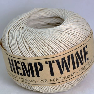 May include: A roll of natural hemp twine with a brown paper label that reads "HEMP TWINE", "NGTH (0.5mm) • 328 FEET (100M) • 100% HEMP F".