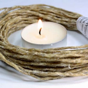 May include: A burning tea light candle is surrounded by a coil of natural-coloured, twisted wick. A label on the wick reads "Organic Bees Wax". The candle and wick are likely for candle making or aromatherapy.
