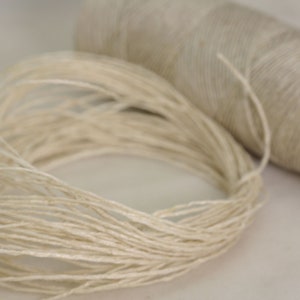 May include: A spool of natural fiber twine, with a loose end of the twine spilling out from the spool.