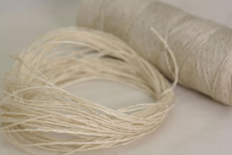 May include: A spool of natural fiber twine, with a loose end of the twine spilling out from the spool.