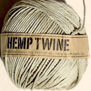 Puede incluir: Una bola de cuerda de cáñamo natural con una etiqueta de papel marrón que dice "HEMP TWINE STRENGTH (2mm) 265 FEET (81 M) 100% HEMP FIBER, 2009".