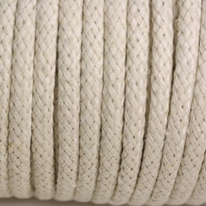 Peut inclure: Gros plan d'une bobine de corde tressée de couleur naturelle. La corde est faite d'une fibre naturelle, peut-être du coton ou du jute, et a une surface légèrement texturée.