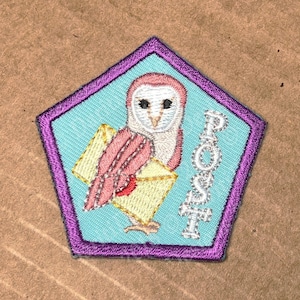 Peut inclure: Écusson brodé en forme de pentagone avec une bordure violette. L'écusson représente un hibou rose et blanc tenant une enveloppe jaune. Le mot "POST" est brodé en argent. Le texte "WoRM Scouts Badge/Patches ©DaritiDesigns" est en haut et en bas.