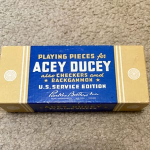 May include: A rectangular box for "Acey Deucey" playing pieces, also for checkers and backgammon. The box has a blue and yellow design with the text "U.S. Service Edition" and the Parker Brothers Inc. logo.