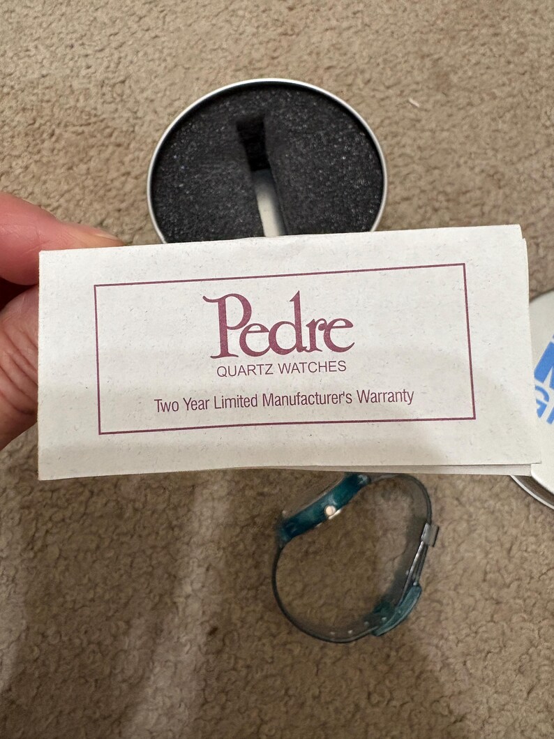 Puede incluir: Un reloj de cuarzo turquesa y plateado con una correa a juego se muestra junto a una tarjeta de garant&iacute;a y una caja de reloj. La tarjeta dice "Pedre Quartz Watches" y "Two Year Limited Manufacturer's Warranty".