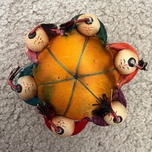 Vintage pin cushion with 6 Chinese characters surrounding it.