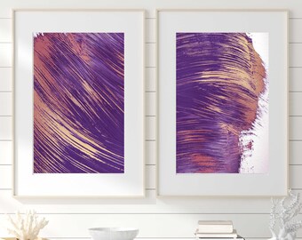 Puede incluir: Dos pinturas abstractas enmarcadas con pinceladas moradas y doradas. Las pinturas están colgadas en una pared blanca sobre una cómoda blanca con dos cajones y tres cestas de mimbre.