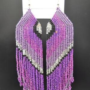 May include: A pair of long, beaded earrings with a purple and silver gradient. The earrings are made of small, round beads and have a fringe-like design.