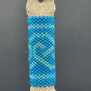 Pode incluir: Um chaveiro de couro com um tassel de franjas, adornado com contas azuis e brancas. O chaveiro tem um anel de metal.