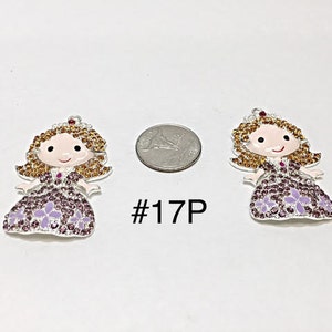 May include: Two princess-shaped charms with silver-colored metal, adorned with rhinestones in shades of purple and gold. The charms have a smiling face and a crown. The text "#17P" is visible.