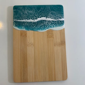 May include: A rectangular bamboo cutting board with a teal and white epoxy resin ocean wave design.