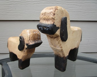 May include: Two wooden carved dog figurines, one larger than the other. Both are painted white with black accents. The larger dog is standing on a glass surface.