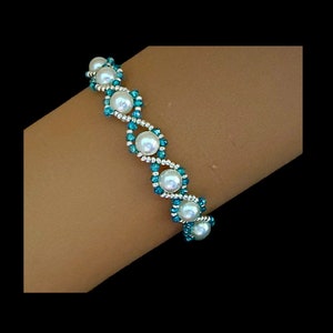 May include: A white pearl and turquoise blue beaded bracelet with a zig-zag pattern.