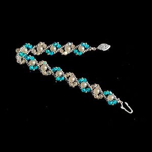 May include: A beaded bracelet with alternating sections of light blue and white beads. The bracelet has a silver-colored clasp and a decorative leaf-shaped charm. The beads are arranged in a repeating pattern.