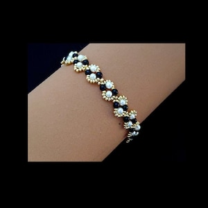 以下が含まれることがあります： 黒と白のビーズブレスレットで、金色のアクセントが施されています。ブレスレットは小さな丸いビーズで作られており、ジグザグ模様になっています。