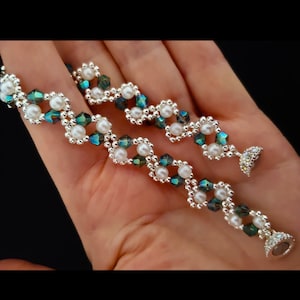 Może przedstawiać: Bransoletka z koralików z naprzemiennymi białymi perełkami i ciemnozielonymi kryształami. Bransoletka ma srebrną klamrę.