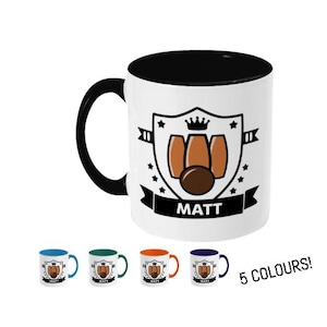 May include: A white ceramic mug with a black rim and handle. The mug features a black and white graphic of a bowling pin with the word "MATT" printed below. The mug is available in five colours: blue, green, orange, red, and black.